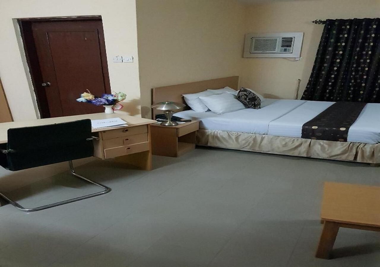 A hotel room with a bed, a desk, a chair, a nightstand, and a small table.