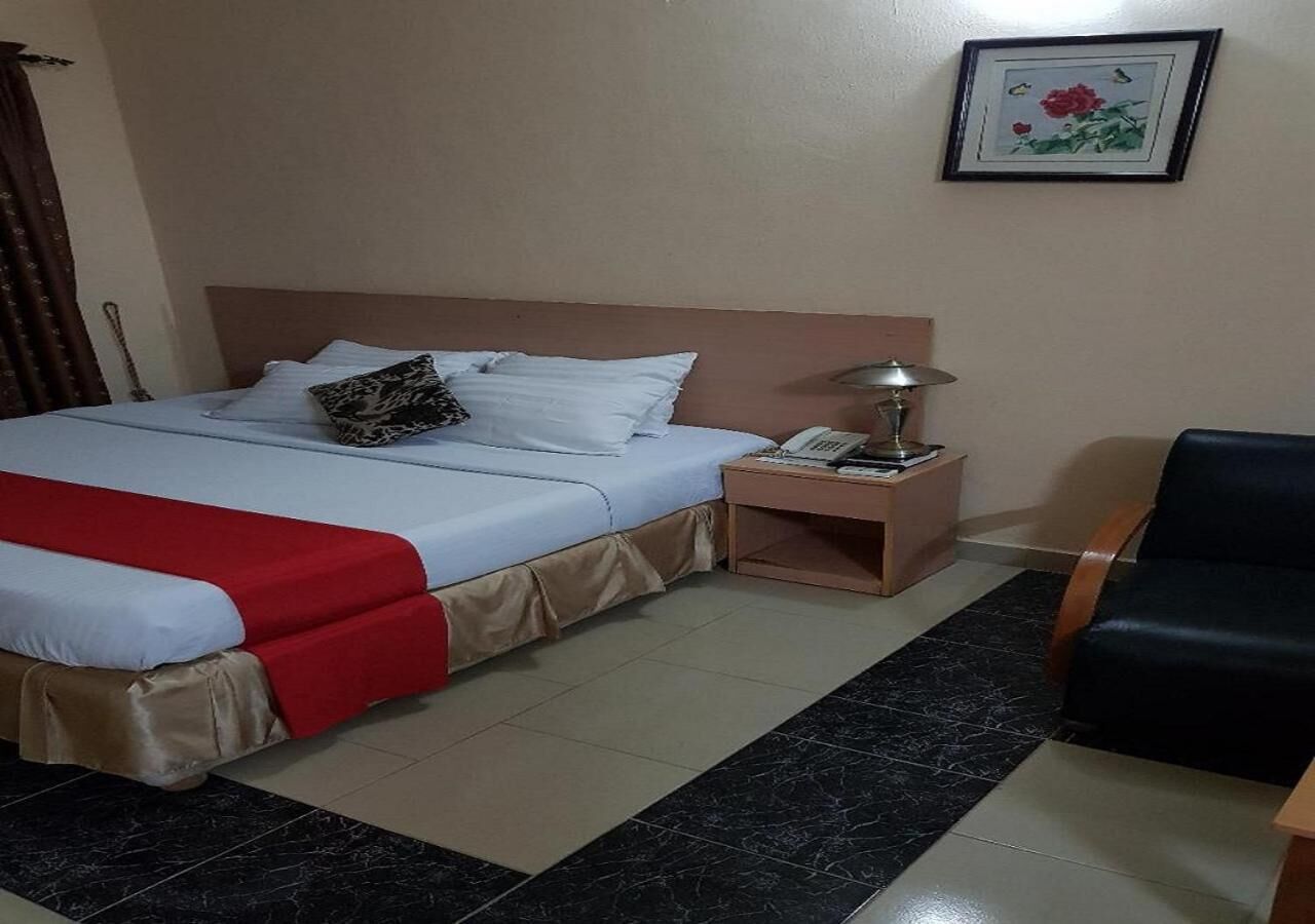 A hotel room with a bed, nightstand, chair, and a framed picture on the wall.