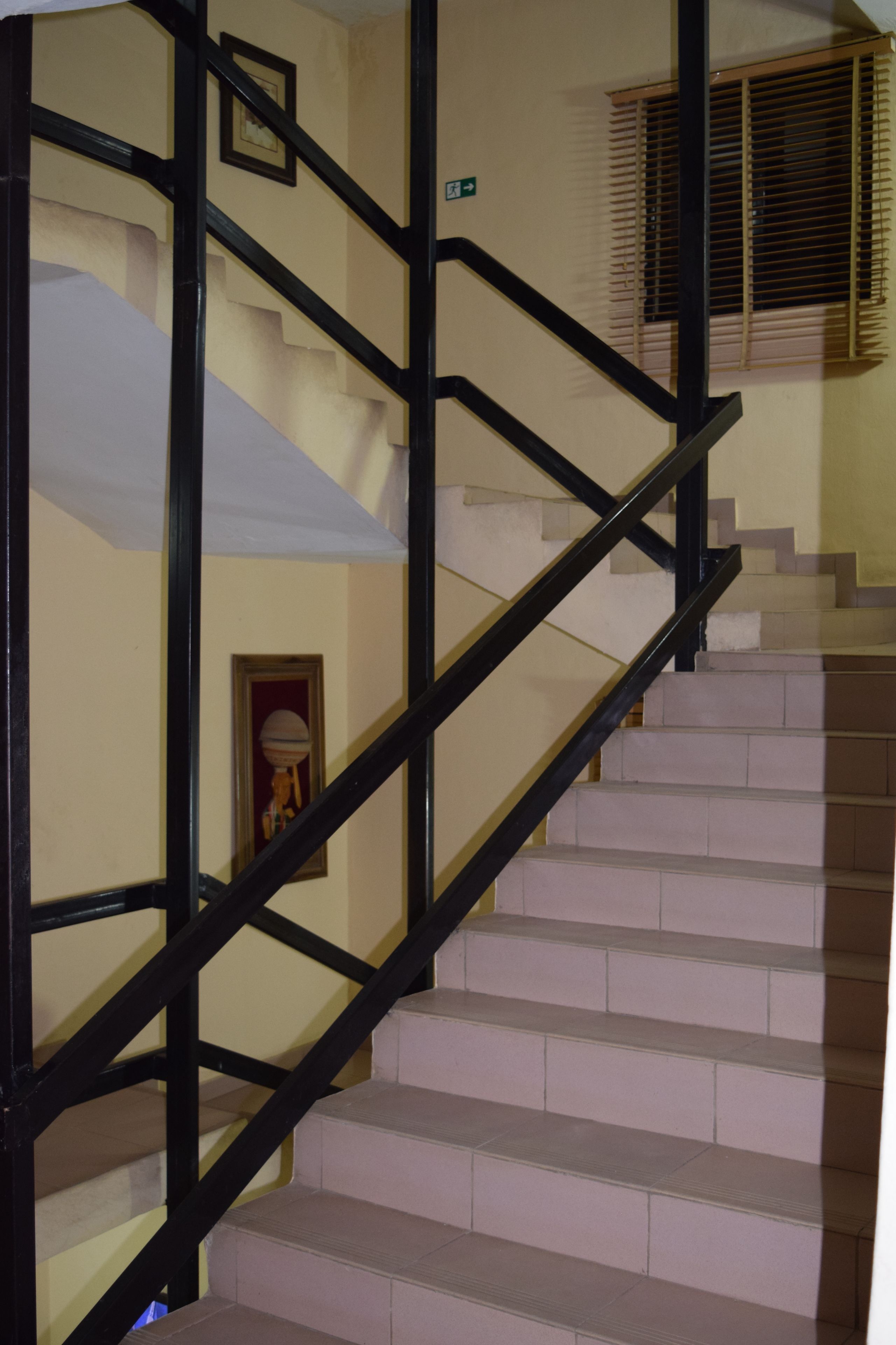 A staircase with black railings and beige steps, leading to a room with a window and a door.