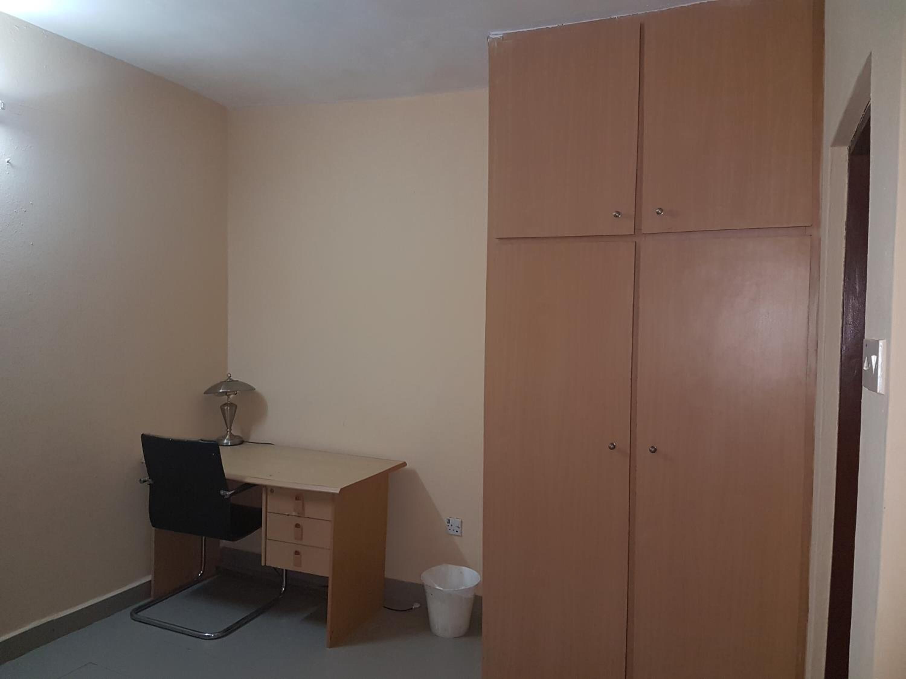 A small room with a wooden wardrobe, a desk with a chair, and a trash bin.