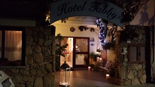 Un arco de piedra con el letrero "Hotel Fabry" sobre una puerta que da a un interior cálidamente iluminado.