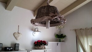 Una habitación con una lámpara de mimbre, un adorno con forma de corazón, una estantería con flores rojas, una radio y un altavoz.