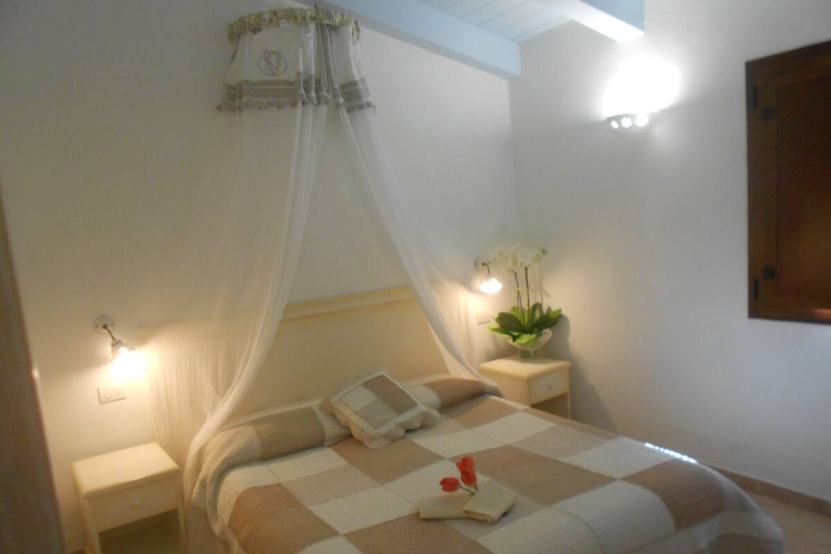 A bedroom with a bed, a nightstand, a bedside table with a lamp, and a wall-mounted light.