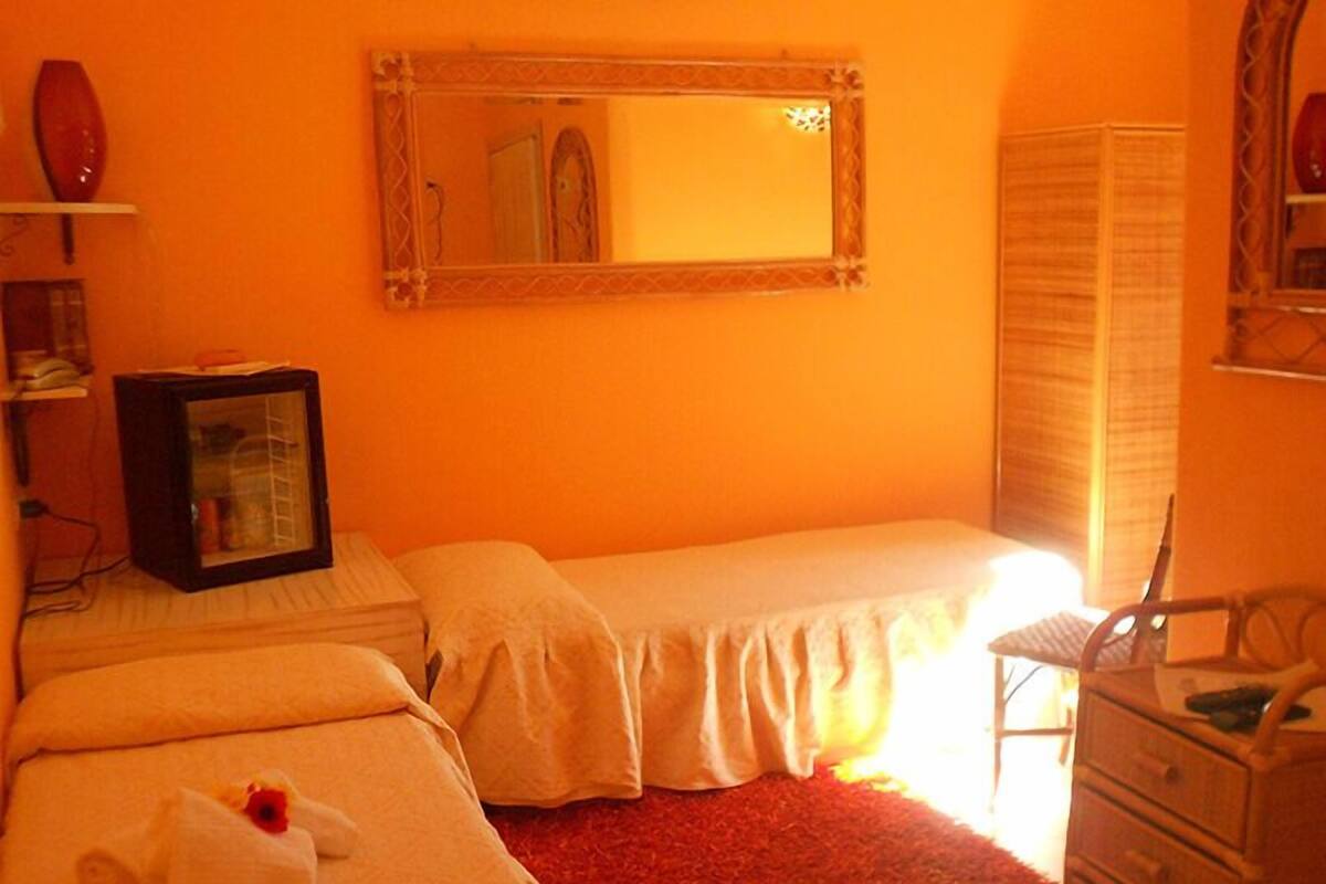 A room with two beds, a mirror, a small cabinet, and a red carpet.