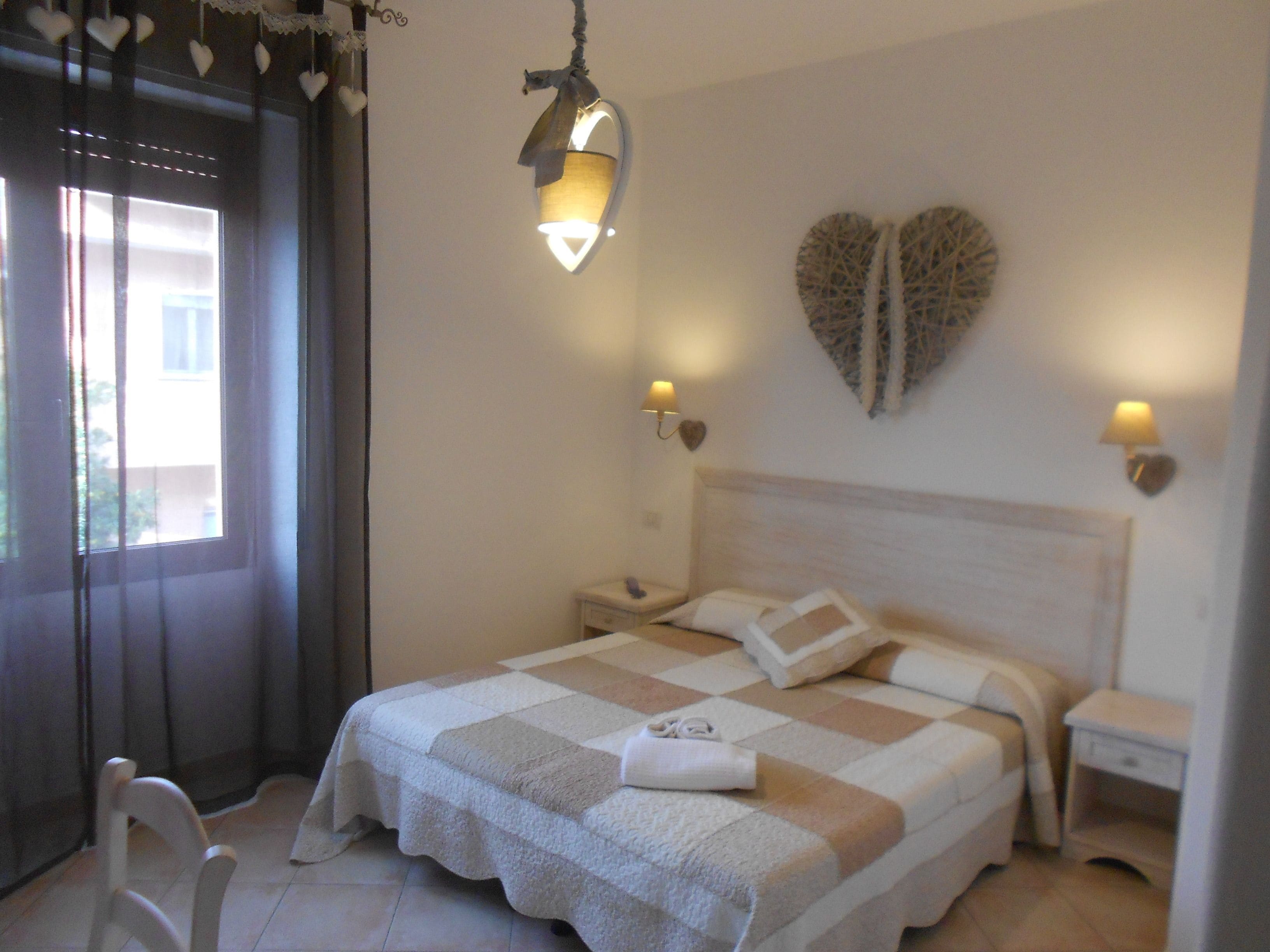 A bedroom with a bed, bedside tables, a chair, and decorative heart-shaped wall art.