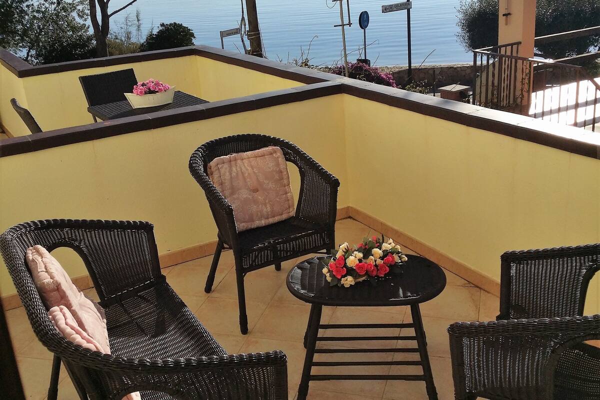 A balcony with wicker furniture, a small table with flowers, and a view of the sea.
