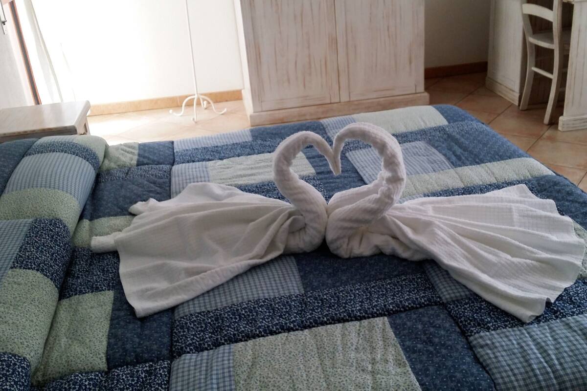 A bed with a blue and white checkered quilt and two white towels arranged in a heart shape.
