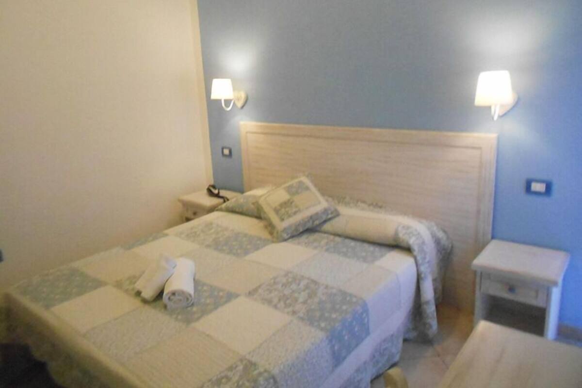 A neatly made bed with a patterned bedspread, two bedside lamps, a nightstand, and a small table with a lamp.