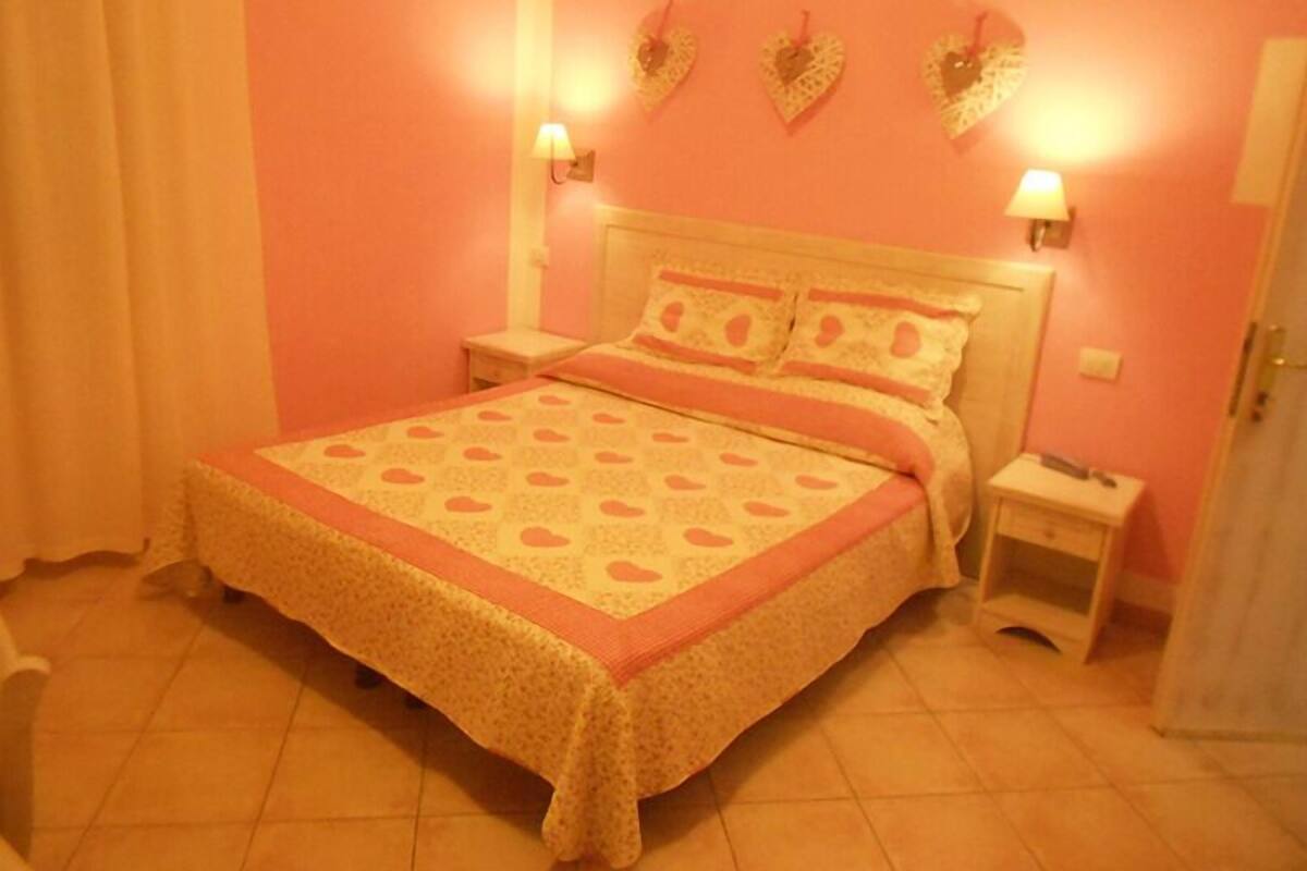 A bedroom with a pink wall, a bed with a patterned bedspread, two bedside tables, and wall-mounted lamps.