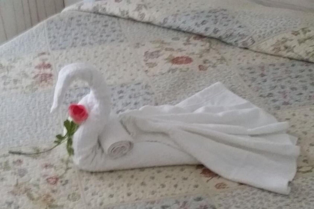 A bed with a floral bedspread and a towel shaped like a swan with a rose.