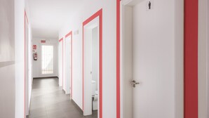 A hotel corridor with white walls and red trim, featuring doors, a fire extinguisher, and a visible toilet. - Tarifa Kite Hostel (Tarifa)