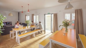 A modern living room with wooden flooring, white and yellow furniture, and large windows with curtains. - Tarifa Kite Hostel (Tarifa)