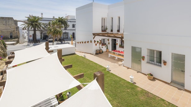 A courtyard with a white building, a wooden deck, and a small seating area. - Tarifa Kite Hostel (Tarifa)
