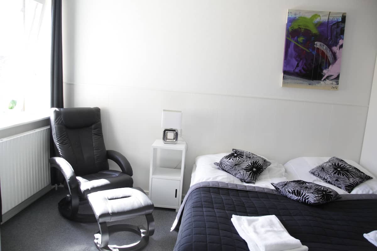 Une chambre d’hôtel avec un lit, une chaise, une table de chevet et un tableau au mur.