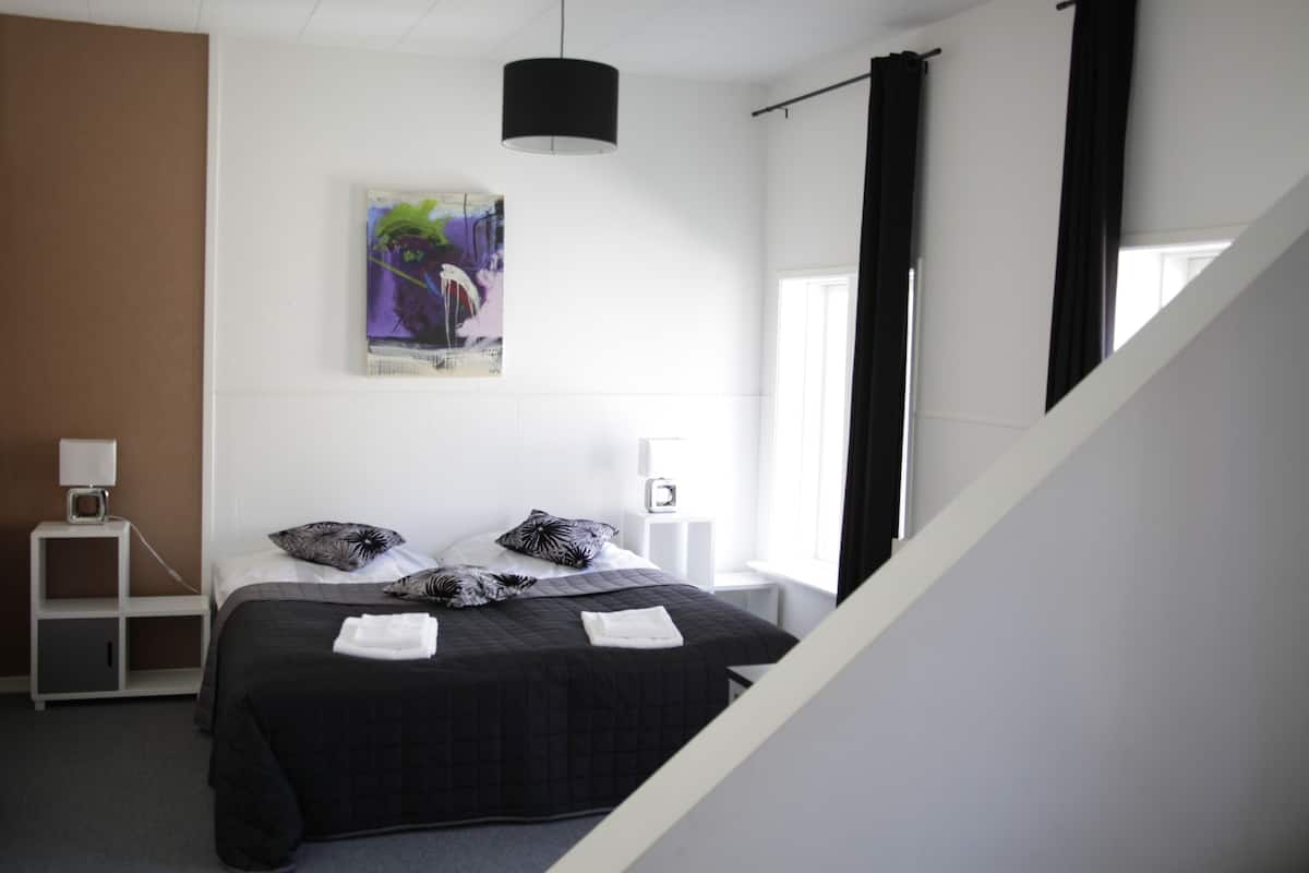Une chambre d’hôtel moderne avec un lit, un tableau, une table de chevet et une fenêtre avec des rideaux.