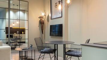 A modern interior with a round table, wire mesh chairs, a flat-screen TV, and pendant lighting.