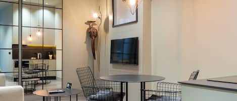 A modern interior with a round table, wire mesh chairs, a flat-screen TV, and pendant lighting.