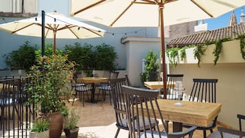 An outdoor patio with multiple tables and chairs, surrounded by potted plants and umbrellas.