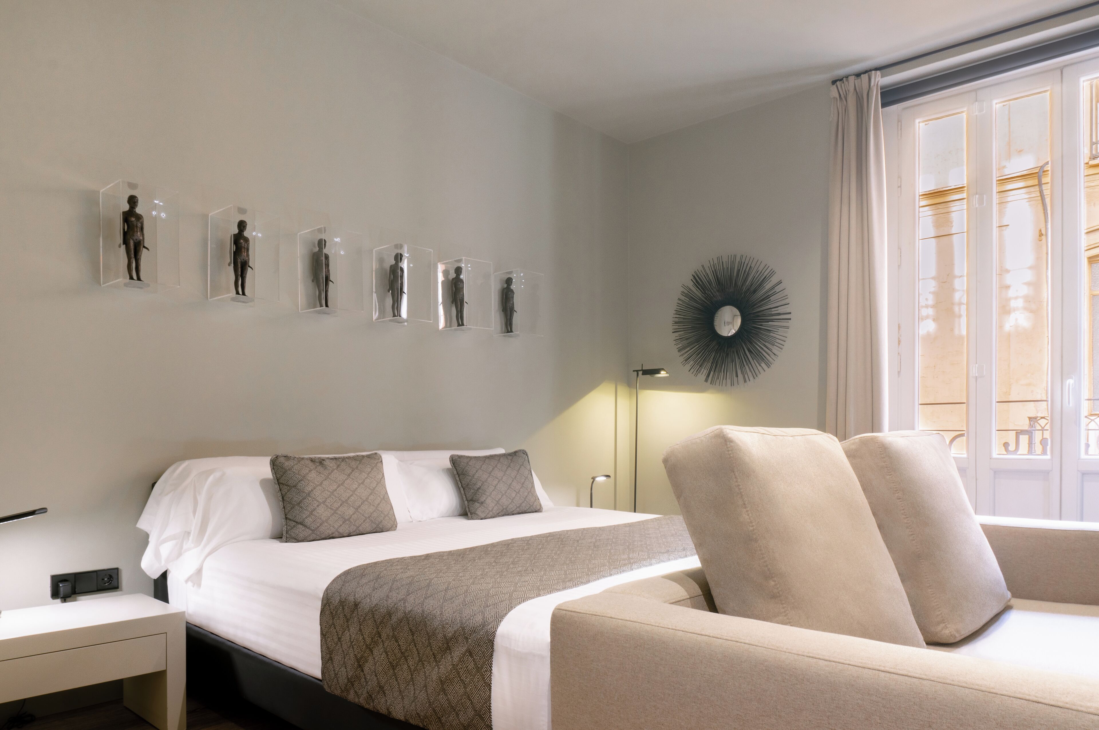 Una habitación de hotel con cama, mesita de noche, una silla y esculturas en la pared.