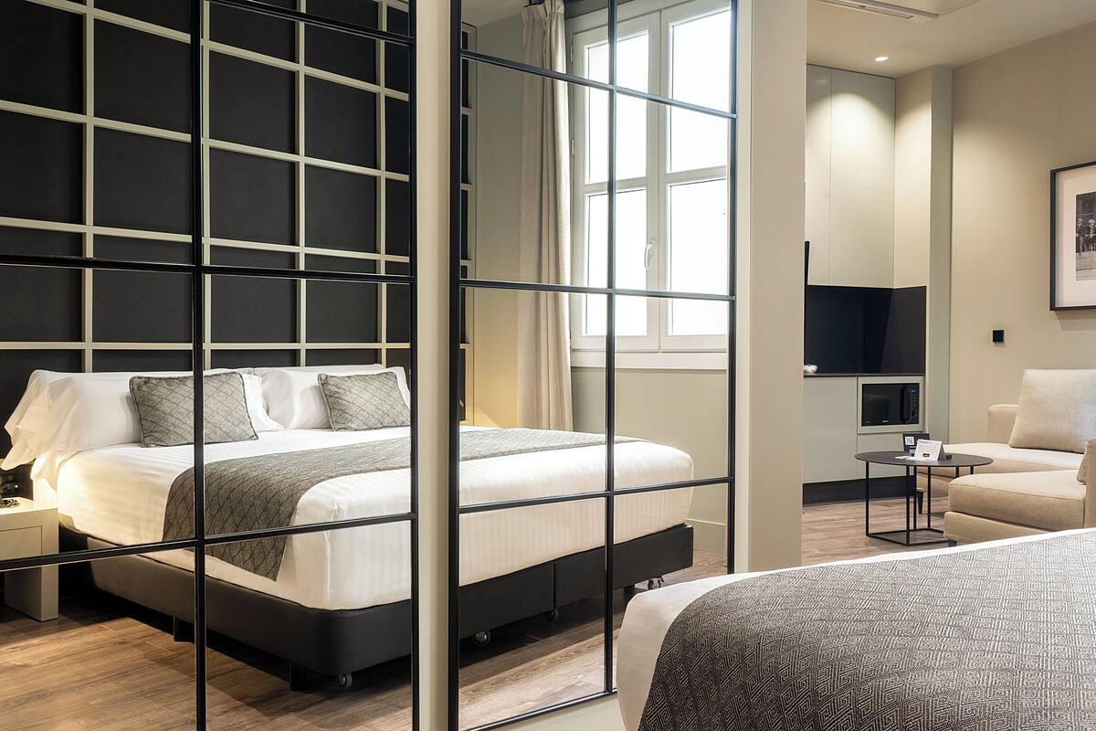 Une chambre d’hôtel moderne avec un grand lit, une table de chevet, un petit bureau, une chaise et une fenêtre avec des rideaux.