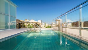 A rooftop swimming pool with glass railings, a clear blue pool, and a view of buildings in the background.