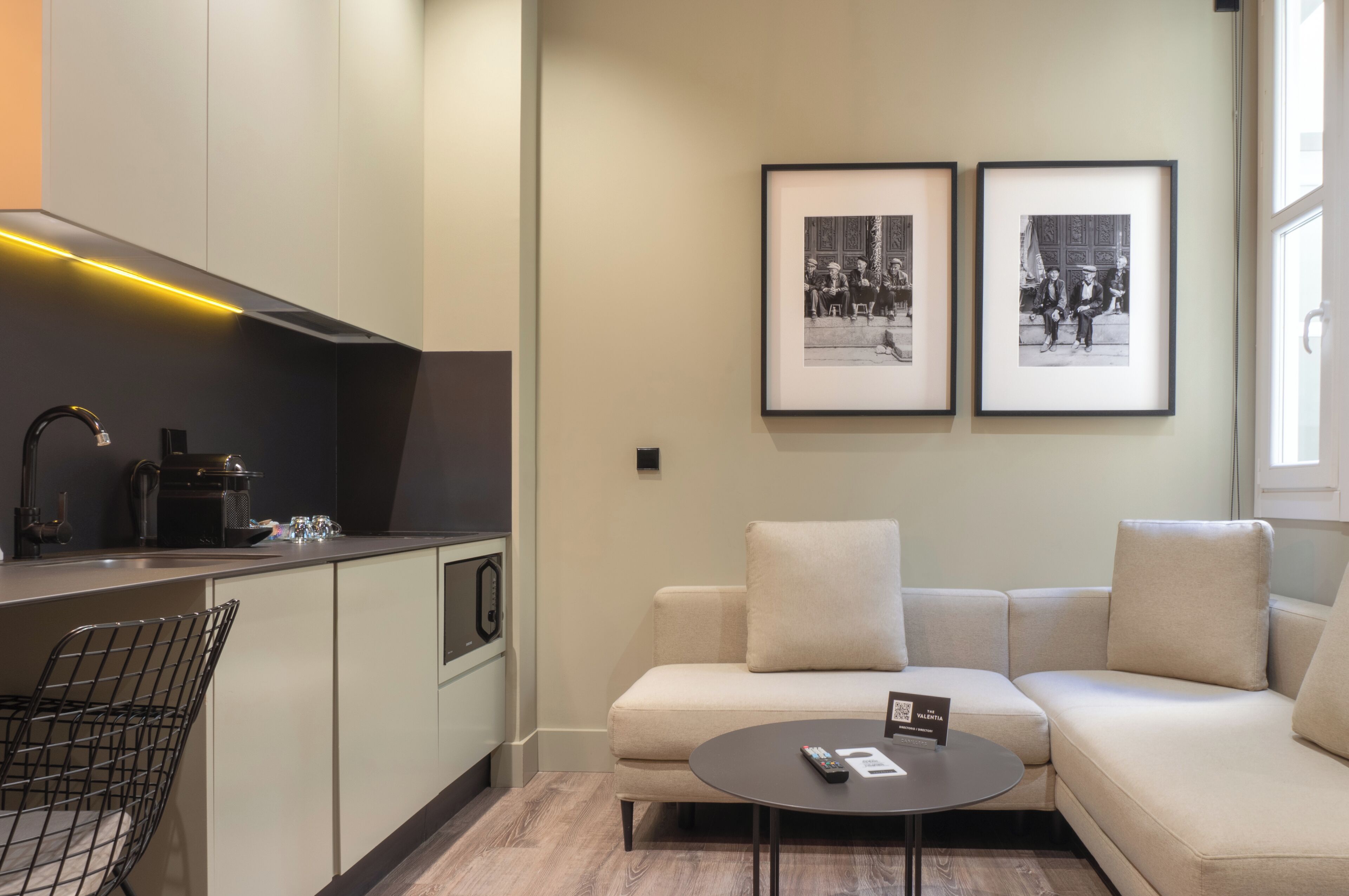 Una cocina moderna con una cafetera, un comedor con un sofá y una mesita, y dos fotografías en blanco y negro enmarcadas en la pared.