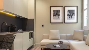 Una cocina moderna con una cafetera, un comedor con un sofá y una mesita, y dos fotografías en blanco y negro enmarcadas en la pared.