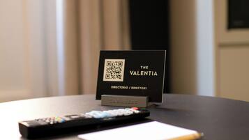 Hotelkamer met een bord waarop 'The Valentina' staat en een QR-code. Op de tafel liggen een afstandsbediening en een notitieboekje.