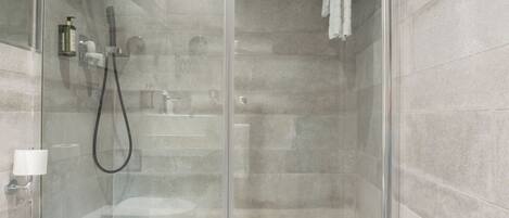 Un baño moderno con mampara de vidrio, cabezal de ducha de mano y dispensador de jabón en la pared.