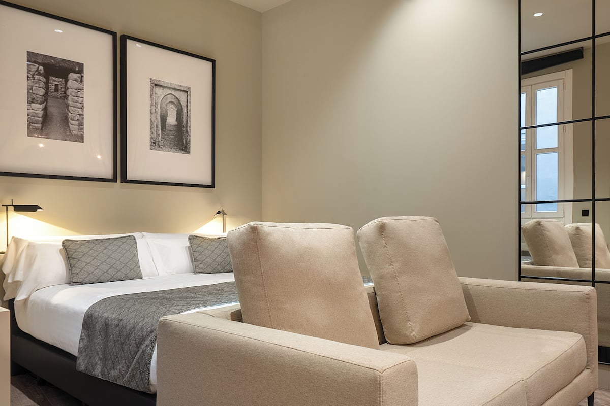 Une chambre à coucher moderne, avec un lit, deux fauteuils, une table de chevet et un miroir.