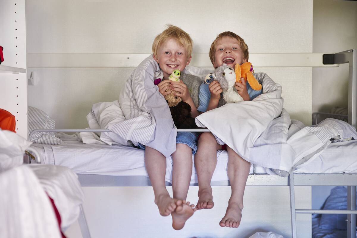 Two children sitting on a bunk bed, holding stuffed animals.