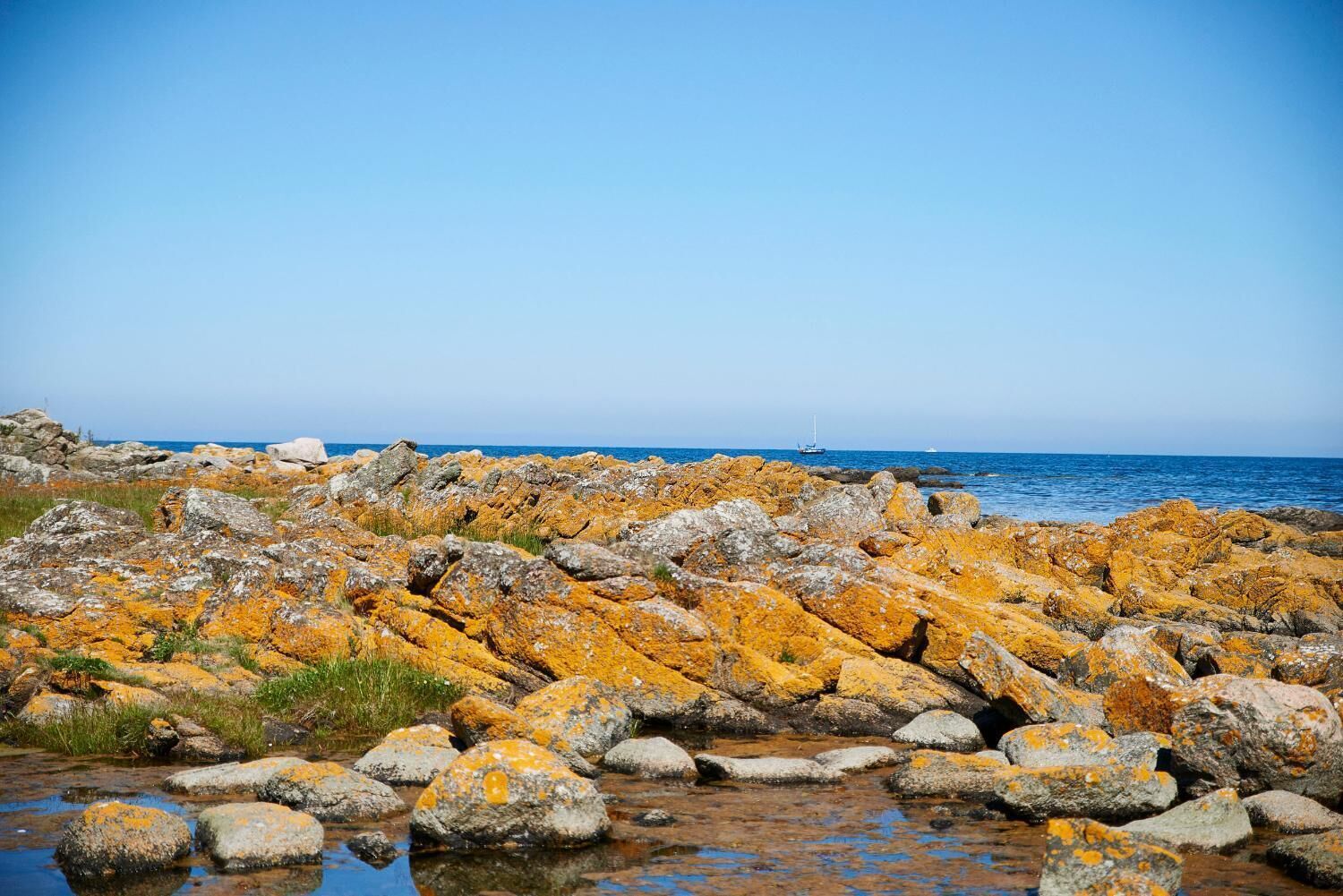 A rocky shoreline with a clear view of the sea and boats in the distance.