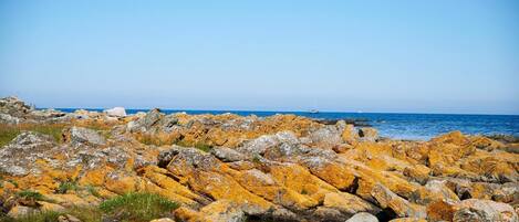 A rocky shoreline with a clear view of the sea and boats in the distance.