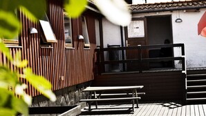 A wooden deck with benches and a building with a sloped roof.