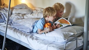 A bunk bed with two children reading a book, one holding an orange toy.