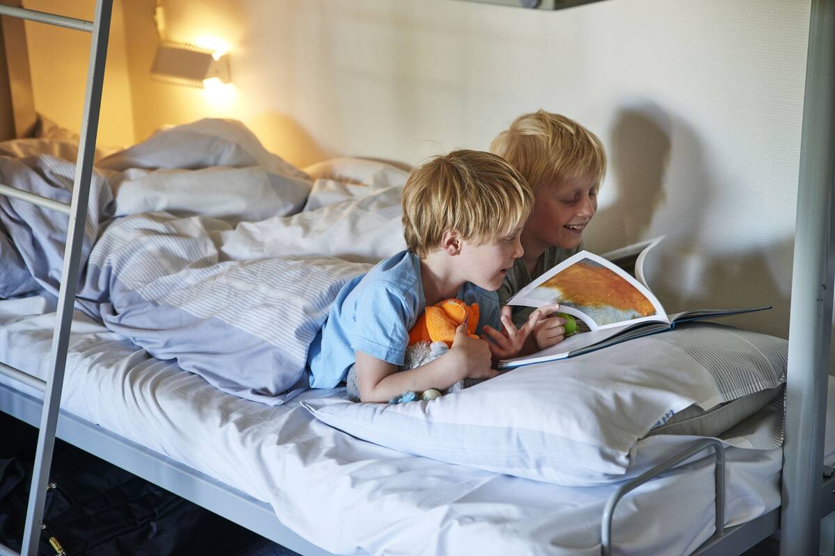 A bunk bed with two children reading a book, one holding an orange toy.