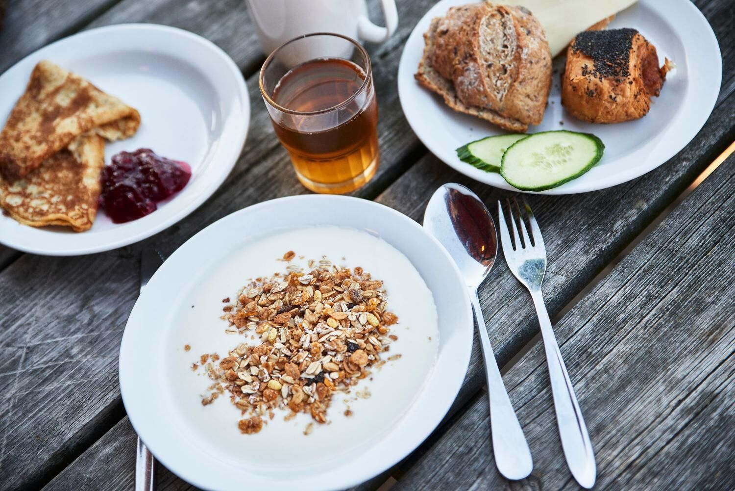 A breakfast setting with pancakes, toast, croissants, and a glass of tea on a wooden table.