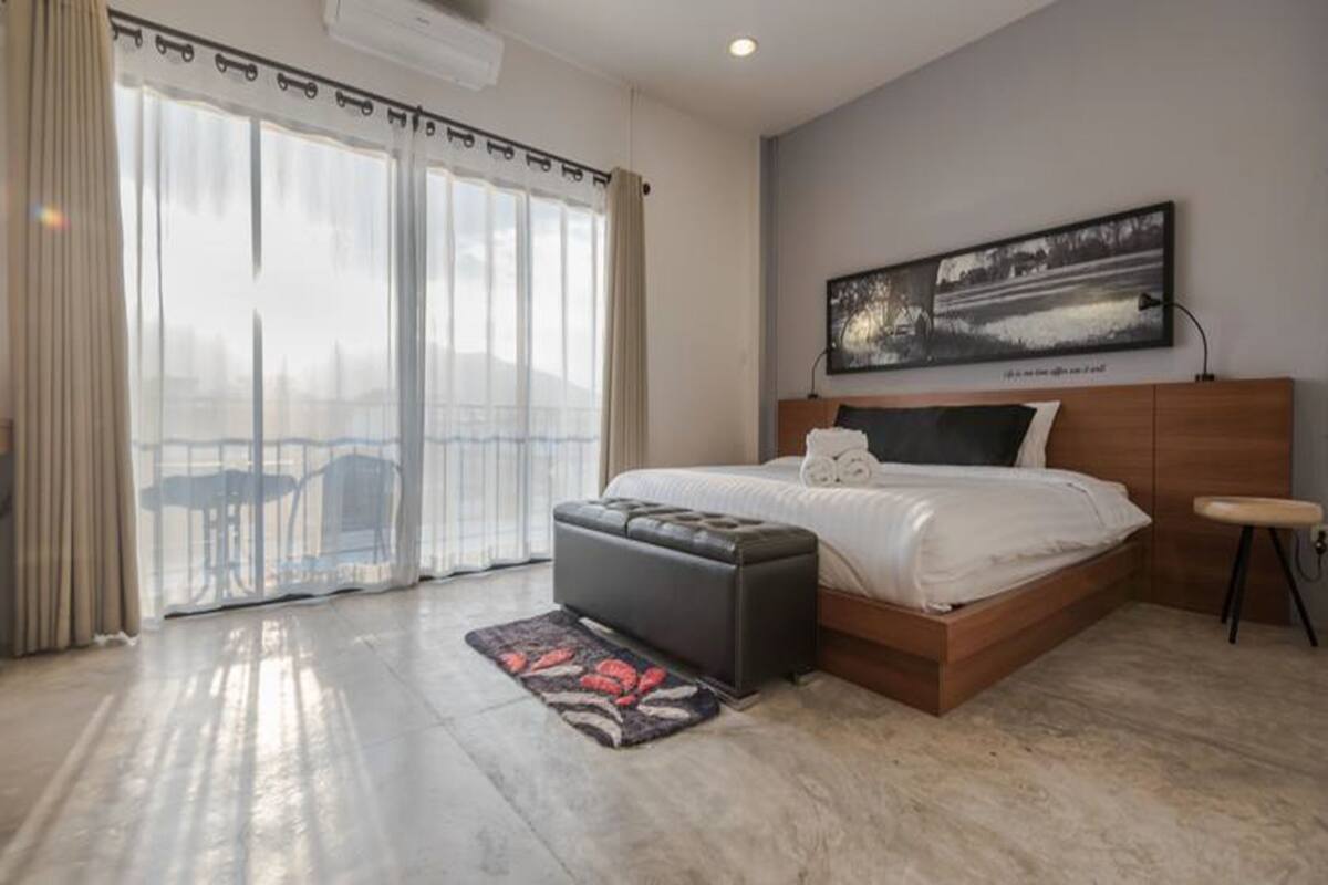 A modern bedroom with a large bed, a bench, a painting, and a view through the window.