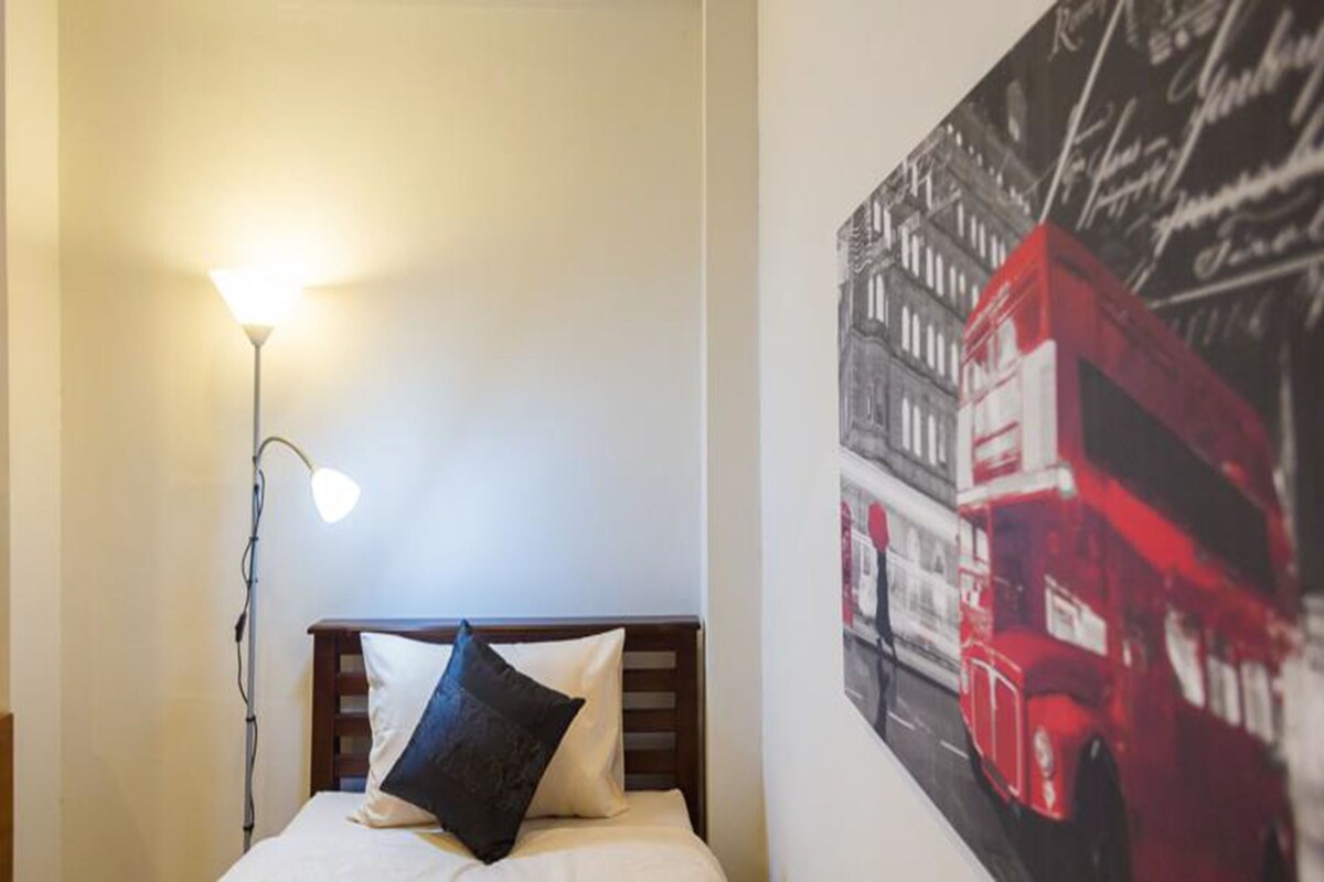 A bed with a headboard, a bedside lamp, and a wall with a black and white photo of a red double-decker bus.