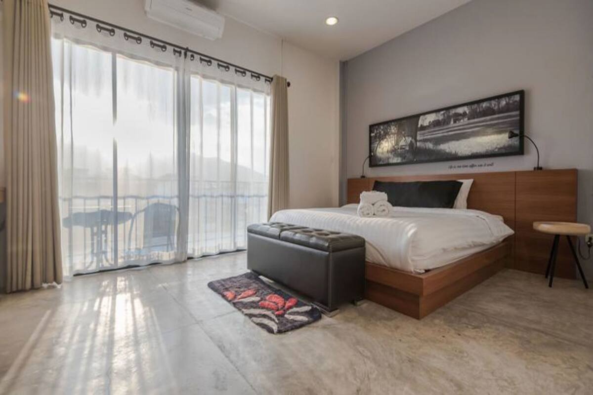 A bedroom with a bed, a wooden headboard, a nightstand, a window with curtains, and a painting on the wall.