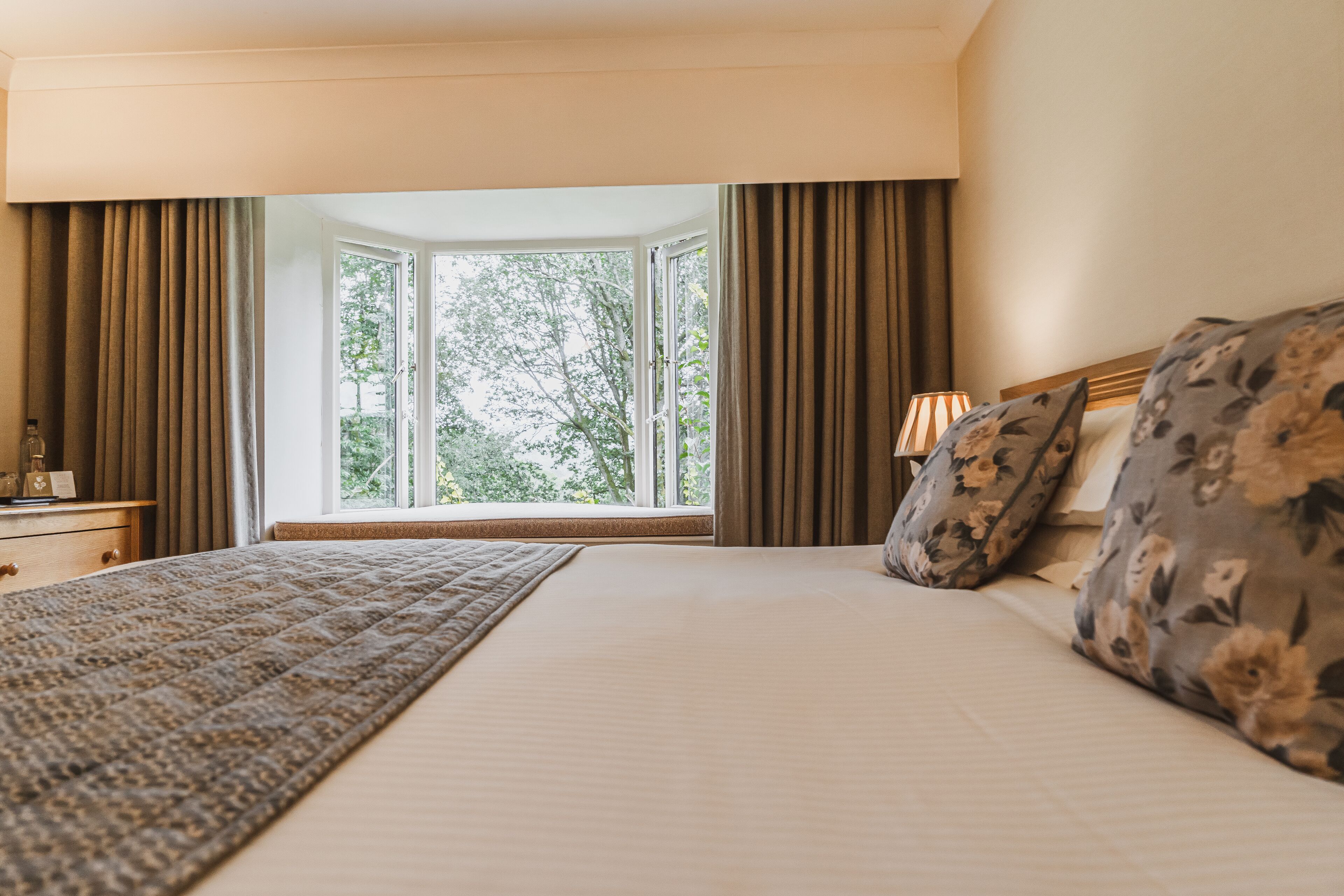 Una camera d'albergo con un letto grande, una finestra con tende, un comodino e una lampada.