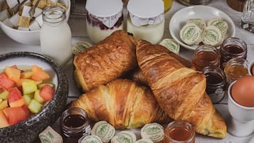 Un desayuno con croissants, fruta, mantequilla y mermelada.