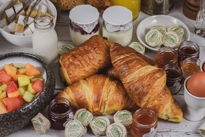 Een ontbijttafel met croissants, fruit, boter en jam.