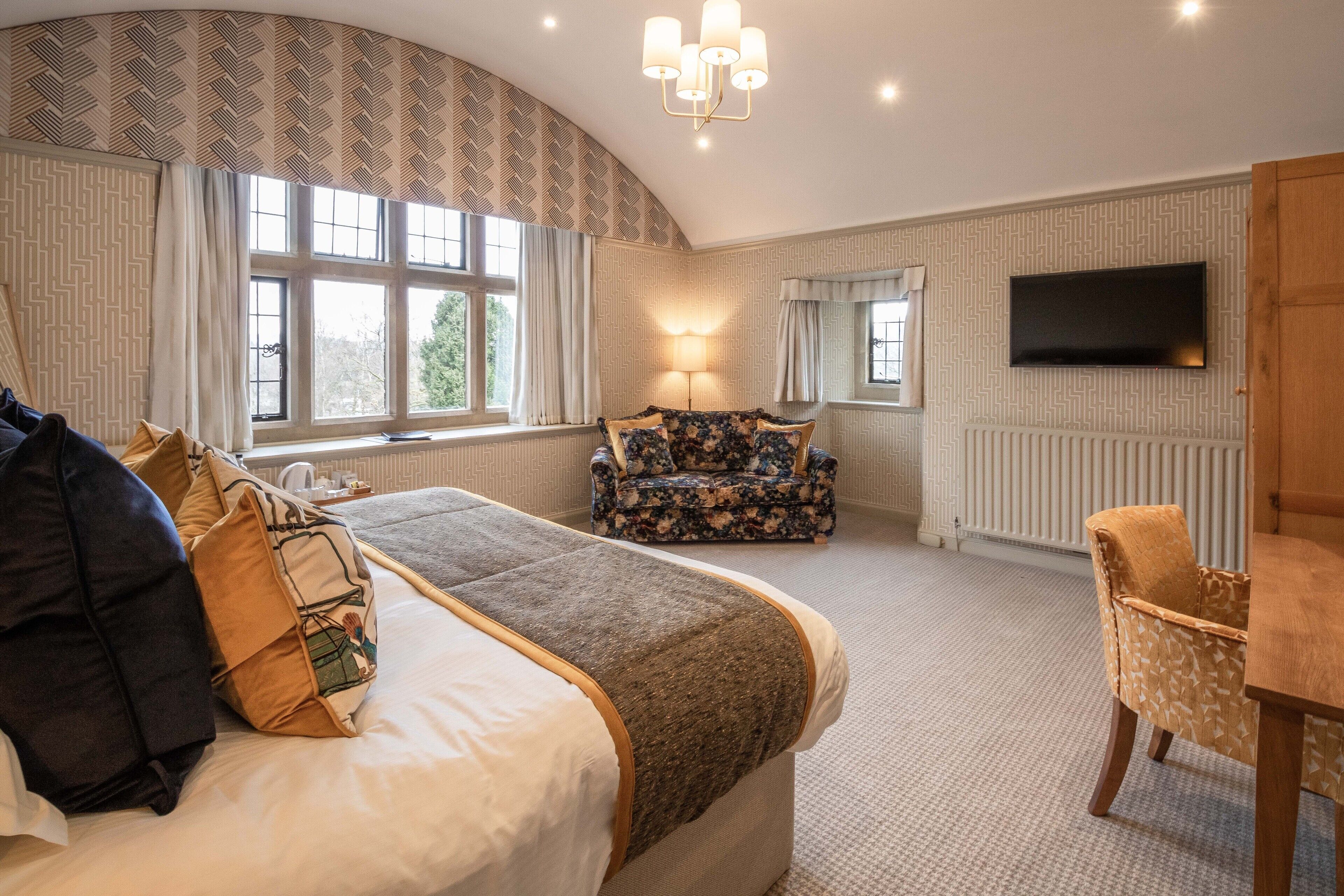 A hotel room with a large bed, a sofa, a TV mounted on the wall, and a window with curtains.