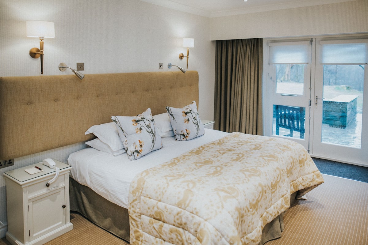 Une chambre d’hôtel avec un grand lit, une table de chevet avec un téléphone et une fenêtre avec des rideaux.