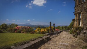 Un edificio de piedra con un patio, mesas al aire libre y vistas a montañas y un lago.