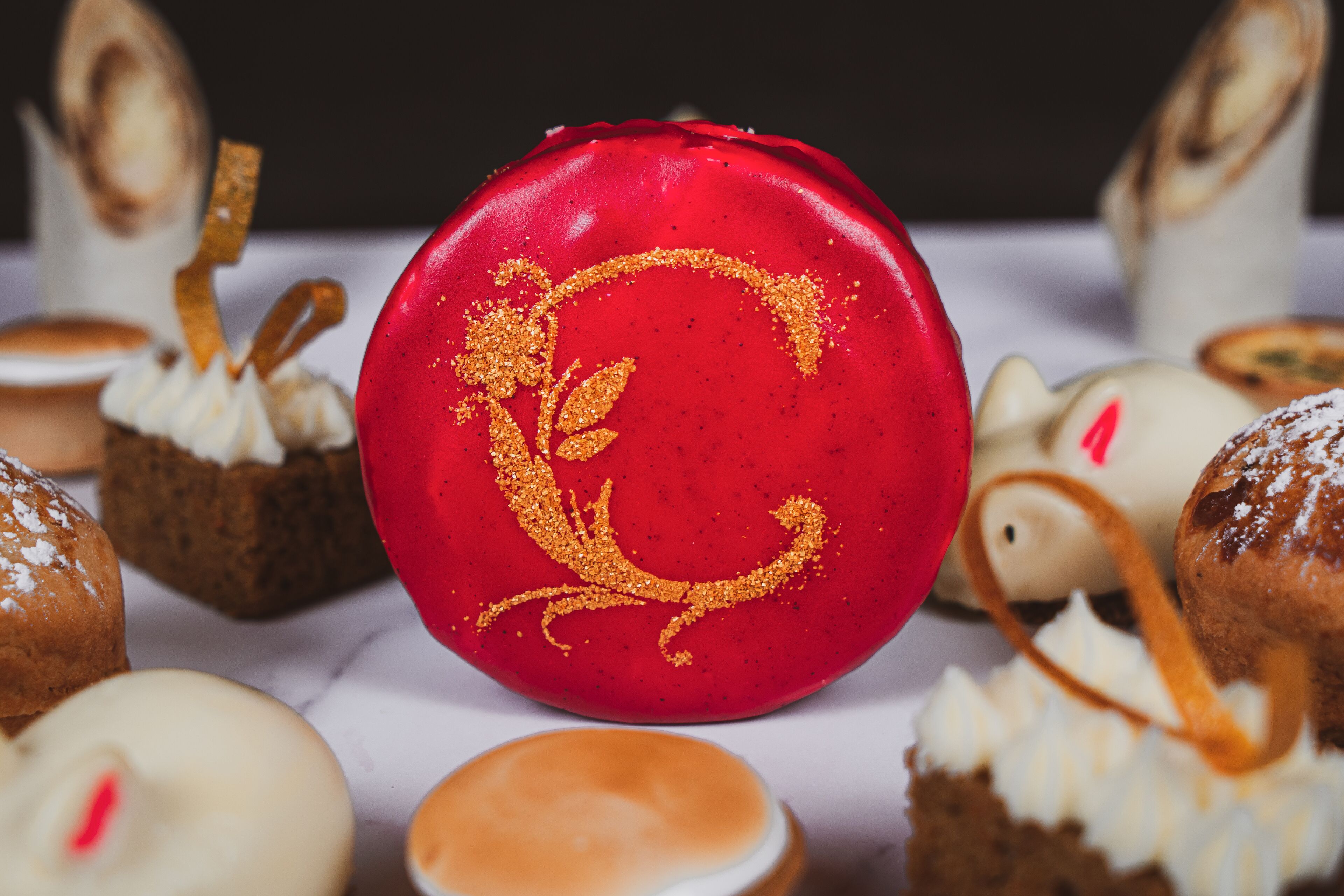A variety of pastries and desserts, including a red cake with a golden design, arranged on a table.