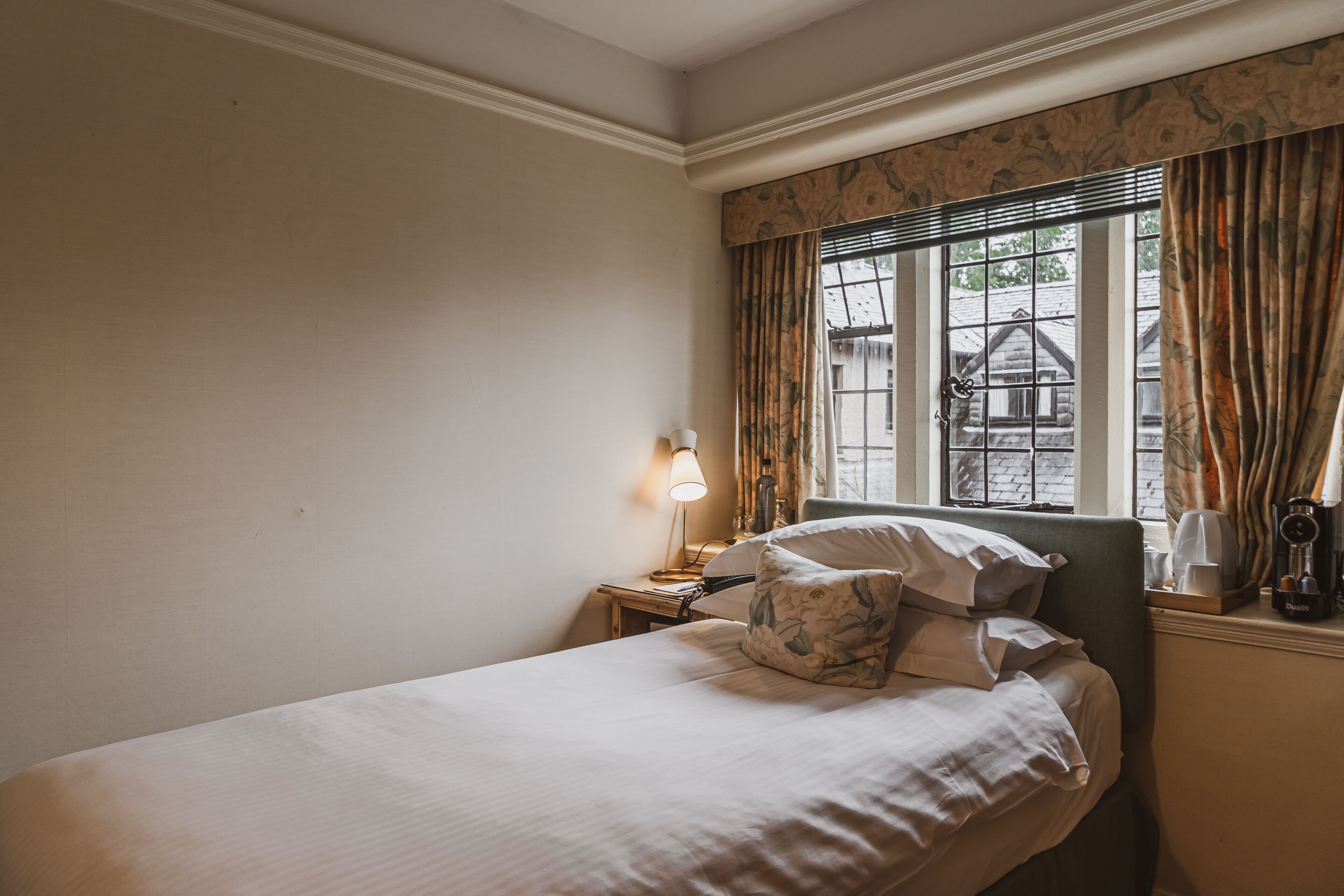 A neatly made bed with pillows, a bedside lamp, and a window with curtains.