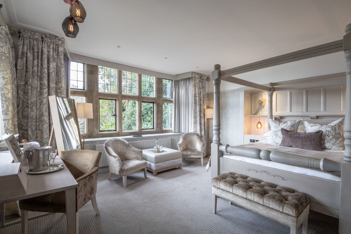 Une chambre spacieuse dotée d’une grande fenêtre, d’un lit à baldaquin et d’un coin salon avec des fauteuils et un banc.
