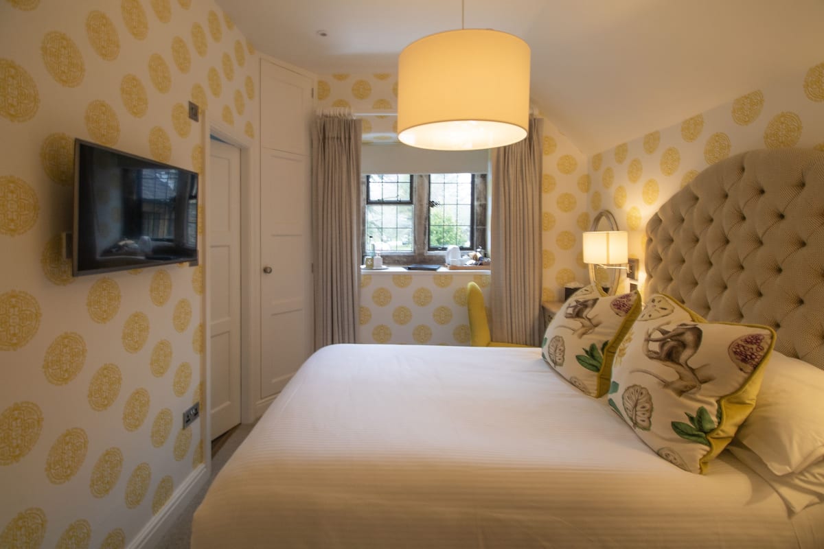 Une chambre avec un grand lit, un téléviseur fixé au mur et une fenêtre avec des rideaux.